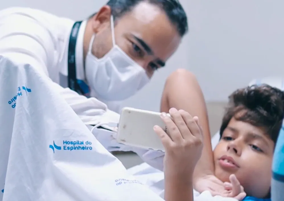 Dr. Áureo de Andrade conversando com um menino em leito hospitalar